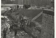 Zdjęcie czarno- białe przedstawiające remont Śluzy Gorczyca w 1953 roku.Na zdjęciu jest mała grupa ludzi- kobiet i mężczyzn- pozująca do zdęcia.